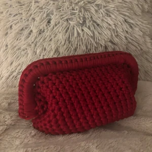 Rad handvirkad clutch  - Säljer en röd handvirkad clutch / handväska som jag har virkat! Väskan är i ett mjukt garn och är väldigt rymlig! Kan bäras i handen som en clutch eller bäras i handtaget.