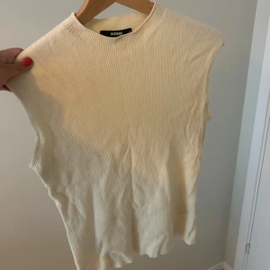 Ribbad ärmlös topp från Bik Bok - Krämvit ribbad topp från Bik Bok med hög hals och ärmlös design. Perfekt att styla med jeans eller kjol för en clean look. Mjuk och stretchig i materialet för en bekväm passform. Endast använd ett fåtal gånger💕