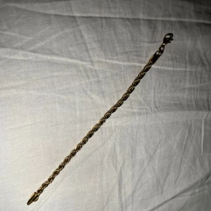 Guldigt tvinnat armband med karbinlås - Snyggt armband i guldig färg med tvinnad kedja och karbinlås. Kedjan har en klassisk rope chain-look som ger en lyxig vibe och passar perfekt till din stil. Enkel att ta på och av tack vare det smidiga låset. Perfekt accessoar för att lyfta din outfit.