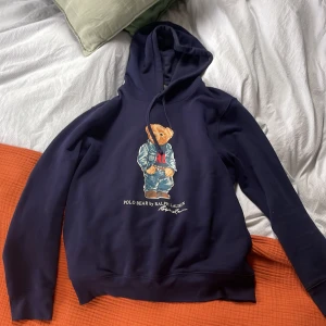 Mörkblå hoodie Polo Bear Ralph Lauren - Mörkblå hoodie från Ralph Lauren med ikoniska Polo Bear-trycket framtill. Tröjan har huva med snörning och lång ärm. Köpt i rl butik för 2700, 9/10 skick. Kan gå ner i pris vid snabb affär