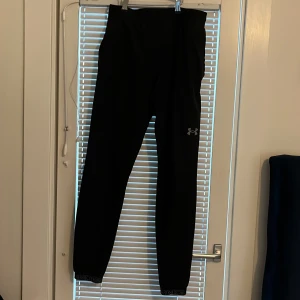 Svarta tränings byxor från Under Armour  - Svarta tränings byxor från Under Armour med elastisk midja och diskret logga på benet. Sitter tight och är perfekta för träning eller chill. Materialet är syntet och de har en clean look utan onödiga detaljer i ganska bra skick som jag säljer för 350