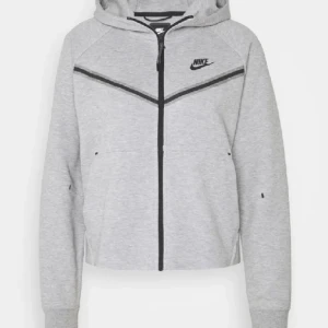 Grå mjukisbyxor från Nike med dragkedja - Snygga ljusgrå mjukisbyxor från Nike med svart logga på benet och cool dragkedjedetalj på sidan. Byxorna har snörning i midjan och är tillverkade i mjukt bomullsmaterial. Perfekta för chill eller träning, med en relaxed och sportig vibe.