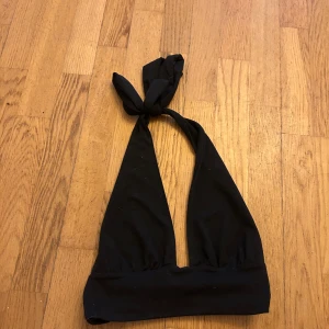 Svart tröja  med knyt - Snygg svart tröja med halterneck och knyt i nacken. Enkel och stilren design med bred resår under bysten för extra stöd. Perfekt för strandhäng eller poolparty.