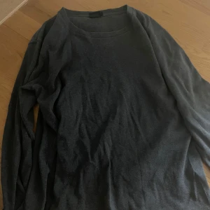 Mörkgrå långärmad tröja från Steel - En basic mörkgrå långärmad tröja från Steel i storlek L. Tröjan har en enkel rund halsringning och är tillverkad i mjukt bomullsmaterial, perfekt för lager-på-lager eller chill dagar. Passar dig som gillar en clean och stilren look.