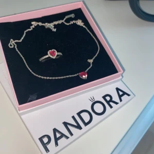Pandora halsband & ring med röda hjärtan - Superfint set från Pandora med ett silverfärgat halsband och matchande ring, båda med röda hjärtformade stenar och små gnistrande detaljer runt om. Perfekt för dig som älskar romantiska smycken med lite extra bling.