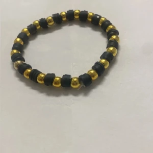 Svart och guldigt pärlarmband - Coolt armband med svarta och guldiga pärlor i rund form. Pärlorna är varvade och sitter på en elastisk tråd, vilket gör det enkelt att ta på och av. Perfekt accessoar för att ge din outfit lite extra edge.