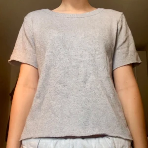 Ljusgrå stickad topp med kort ärm - En enkel och stilren ljusgrå stickad topp med rund halsringning och korta ärmar. Perfekt för dig som gillar en avslappnad och clean look. Mjuk och skön mot huden.
