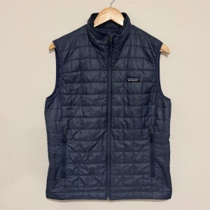Mörkblå dunväst från Patagonia - Snygg mörkblå dunväst från Patagonia med quiltad design och hög krage. Superfint skick, skulle säga 8/10. Nypris 1900 kr.