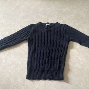 Svart kabelstickad tröja Gina Tricot - Kabelstickad mörkblå tröja från Gina Tricot i storlek XS. Tröjan har rund halsringning, långa ärmar och ribbade muddar vid ärmslut och nederkant. Perfekt för lager-på-lager och snygg till både jeans och kjol.