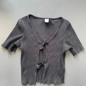 Svart ribbad knytblus från Lindex - Svart ribbad blus från Lindex med korta ärmar och v-ringning. Toppen har två snygga knyt framtill och är tillverkad i mjuk bomull. Står kids men passar xxs-xs eftersom den är stretchig! 💕
