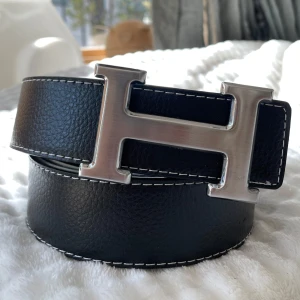H Bälte Svart - Säljer ett svart bälte med ett silvrigt snyggt ”H” spänne. Bältet har en längd på 105 cm (storlek 42) och är Inte använt en enda gång, tveka inte att fråga! 💯👌