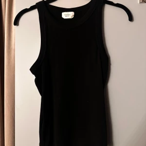 Svart linnetopp från Gina Tricot - En svart, klassisk linnetopp från Gina Tricot, basically basics-kollektionen. Toppen är ärmlös med rund halsringning och har en tight passform. Perfekt att styla med jeans eller kjol för en clean look.