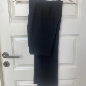 Svarta kostymbyxor i klassisk modell - Snygga svarta kostymbyxor med raka ben och pressveck samt diskreta bakfickor. Riktigt bekvämt material! Användt en gång sen har den tyvärr bara legat i skåpet:)