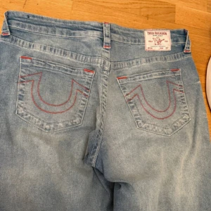 True Religion Bobbi Low Slung Baggy Jeans - Säljer ett par ljusblåa True Religion Bobbi Low Slung Baggy jeans med klassiska röda sömmar på bakfickorna. Jeansen har en lös och baggy passform med låg midja och breda ben. Perfekta för en avslappnad och trendig stil. Pris går att diskutera. Helt nya använda en gång.