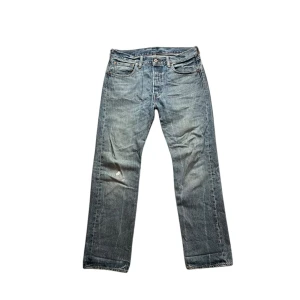 Levi's 501 jeans - Klassiska blå Levi's 501 jeans med raka ben och knappgylf. Jeansen har fem fickor och en vintage tvättad look. Tillverkade i 100% bomull och har den ikoniska läderpatchen bak i midjan. Som du ser på bild 5 så har jeansen ett litet hål på vänstra benet.