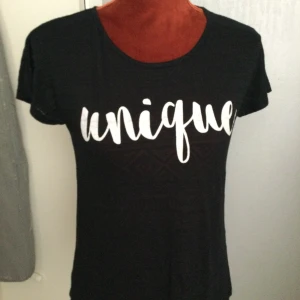 Svart t-shirt med tryck från Club XPRS S - Svart t-shirt med vitt tryck 'unique' på bröstet. Ärmarna har ett diskret mönster i tyget som ger en cool detalj. Rund halsringning och klassisk passform. Perfekt för dig som vill sticka ut lite extra. 65% polyester 35% bomull Svart med tryck. Katter finns i hemmet! 