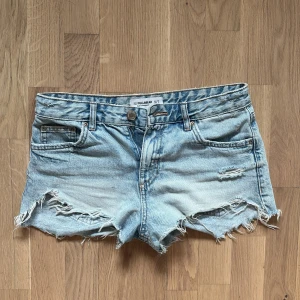 Ljusblå jeansshorts med fransar från Pull&Bear - Säljer ett par lågmidjade ljusblå jeansshorts från Pull&Bear med slitna detaljer och fransig kant. Klassisk femficksmodell med knapp och dragkedja framtill. Pris kan diskuteras!💓