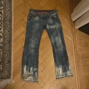 Blå bootcut jeans med blekta detaljer - Säljer ett par blå bootcut jeans med tydliga blekta partier och slitna detaljer. Jeansen är, låg midja och utsvängda . Väldigt coola jeans!!