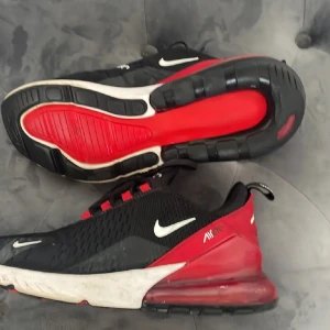 Röda/svarta 270  - Säljer ett par Nike Air Max 270 sneakers i svart och rött med vita detaljer. Skorna har snörning, rund tå och en tydlig Air Max-sula baktill. Perfekta för dig som gillar sportig och modern stil.