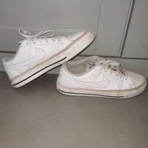 Vita Nike sneakers med snörning - Säljer ett par klassiska vita Nike sneakers med snörning och låg profil. Skorna har vit sula med svart rand och diskret Nike-logga på sidan samt bak. Insidan är ljusgrön. Perfekta för en clean och sportig look. Nytt pris 500