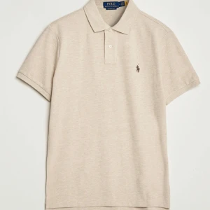 Beige pikétröja från Polo Ralph Lauren - Klassisk beige pikétröja från Polo Ralph Lauren med korta ärmar och krage. Tröjan har två knappar vid halsen och den ikoniska broderade loggan på bröstet. Perfekt för en stilren och avslappnad look. Finns i flera storlekar så det är bara att skriva din storlek så fixar jag det! 