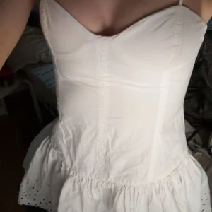 Vit kort klänning med smala axelband från Zara - Supersöt vit klänning från Zara med smala axelband och markerad byst. Klänningen har en lätt utställd kjol med broderade detaljer längst ner. Kommer tyvärr inte till användning längre 🩷🩷