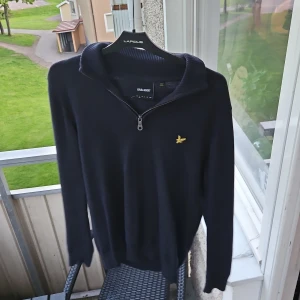Mörkblå tröja med dragkedja från Lyle & Scott - Snygg mörkblå långärmad tröja från Lyle & Scott med halv dragkedja och klassisk gul logga på bröstet. Perfekt för en stilren och avslappnad look. Mjuk och bekväm, passar till mycket. Ribbad Krage, nästintill nyskick