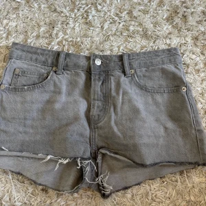 Grå jeansshorts med fransar från 157 - Gråa jeansshorts från 157 med råa fransade kanter och klassisk femficksdesign. Modellen heter LEXI och har en avslappnad passform. Perfekta för varma dagar när du vill ha en cool och enkel stil.