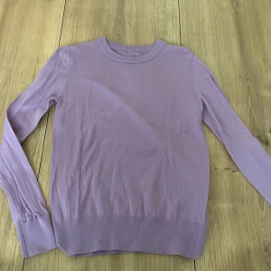 Ljuslila stickad tröja - Säljer en stilren ljuslila stickad tröja med rund halsringning. Tröjan har långa ärmar och ribbade muddar vid ärmslut och nederkant. Perfekt för lager-på-lager under kyligare dagar.