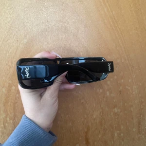 Svarta solglasögon från YSL vintage - Säljer ett par svarta solglasögon från YSL med bred båge och vintage/sportig design. Passar både man & kvinna. Storleken har tyvärr suddats ut i skalmen men skulle tippa på runt 55-18 eller uppåt. 