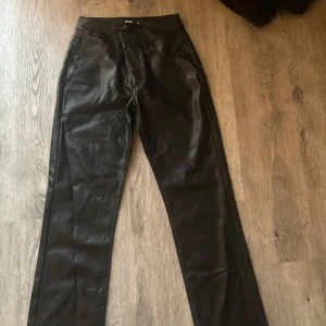 Svarta skinnbyxor med raka ben - Snygga svarta byxor i skinnimitation med låg midja och raka ben. Perfekta för att lyfta vilken outfit som helst. Klassisk design utan synliga detaljer för en stilren look.