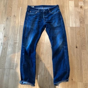 Levi's 501 Premium blå jeans - Säljer ett par klassiska blå Levi's 501 Premium jeans med med rak passform. De är tillverkade i slitstarkt denim. Perfekta för dig som gillar tidlös stil och vill ha ett par jeans som funkar till det mesta. Riktigt snygga slitningar men vid anklarna är de slitna så brukar ha de uppvikta. Går även att sy om man vill. 