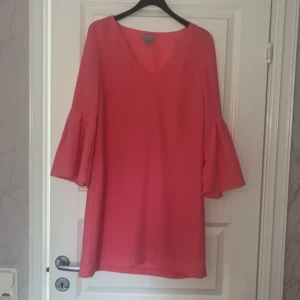 Rosa klänning med v-ringning och volangtärmar - Säljer en rosa klänning från h&m med v-ringning och vida volangärmar. Klänningen har en rak passform och är tillverkad i ett lätt, slätt material. Perfekt för dig som vill ha en enkel men snygg look.