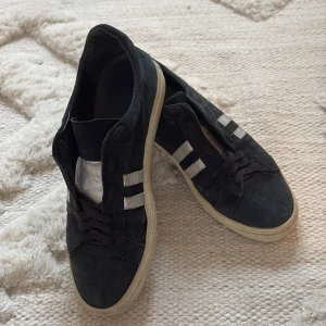 Svarta sneakers med silvriga ränder  - Svarta mocka imitation, sneakers med silvriga detaljer på sidorna och svart snörning. Skorna har en vit sula och är tillverkade i syntetmaterial. Vintage köpta second hand i Paris. Storlek 40 mer som st 41