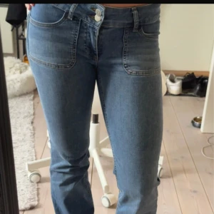 Blå bootcut jeans  - Säljer ett par blå bootcut jeans från Nelly i storlek S med låg midja och snygga fickor bak med lock och knappdetaljer. Perfekta för en avslappnad och trendig look.  Använd några gånger men lite upptrampade där bak(se sista bilden). Men sens inte mycket.