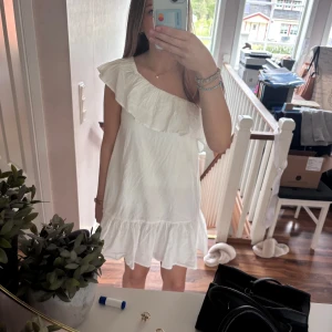 Vit oneshoulder klänning med volang - Säljer en söt vit oneshoulder klänning med volangdetalj över axeln och nertill. Klänningen har en luftig passform och är perfekt för varma dagar. Superfin till sommaren! Är i storlek 152 men passa mig som har xs/s jätte bra. Skriv för mer bilder💕
