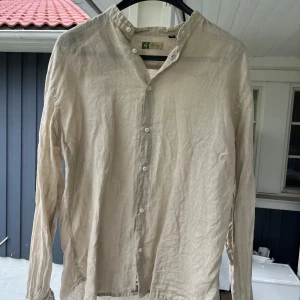 Beige linneskjorta från William - Säljer en stilren beige skjorta från William, tillverkad i Italien. Skjortan är i luftigt linne med lång ärm och knappar framtill. 
