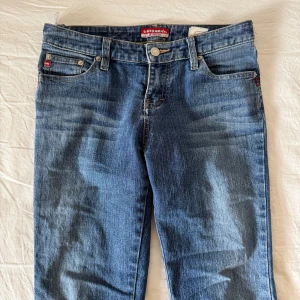 Blå bootcut jeans lågmidjade - Säljer ett par klassiska blå bootcut jeans från Replay med fem fickor och stretch. Jeansen har normal passform och är tillverkade i bomullsmix med polyester och spandex för extra komfort. Perfekta för dig som gillar retrostil.