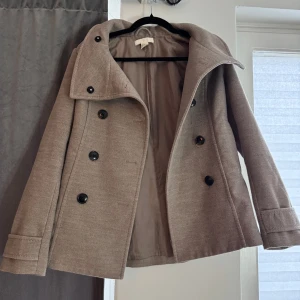 Beige kappa  - Säljer denna kappa då den inte kommer till användning. Fin färg, krage och fina detaljer på ryggen och ärmarna,  är även perfekt till våren och hösten. Använd fåtal gånger och inga defekter. 