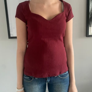 Vinröd ribbad topp med v-ringning - Säljer en vinröd ribbad topp från Anna Field med v-ringning och korta ärmar. Toppen har en figurnära passform och är tillverkad i ett stretchigt material som sitter snyggt på kroppen.