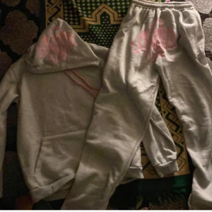 Gråa mjukisbyxor och hoddie med rosa tryck - Säljer ett par gråa mjukisbyxor och hoddie med rosa grafiskt tryck på ena benet. Byxorna har resår i midjan och mudd vid bensluten, samt är gjorda i mjukt bomullsmaterial. Perfekta för chill eller träning. Säljer den för 600 men går ner till 500 snabbaffär samma dag. Byter även mot endast burberry hoodies