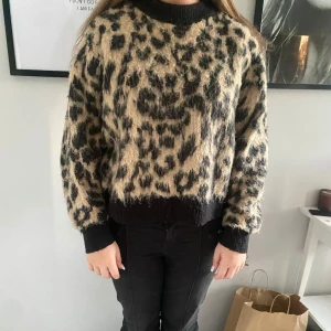 Leopardmönstrad stickad tröja från Other stories  - Säljer en fluffig stickad tröja från other stories med leopardmönster i beige och svart. Tröjan har långa ärmar, breda muddar och en rund halsringning. 
