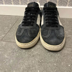 Valentino flycrew  - Snygga sneakers från Valentino i mörkblå mocka med vita skinnpaneler och svarta skosnören. Skorna har rund tå, platt sula och coola nitar på sidan av sulan. Perfekta för dig som gillar exklusiva och stilrena sneakers. Dustbag ingår, 9 nitar borta totalt!