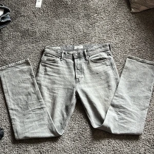 Grå jeans Loose/Chris från Jack & Jones - Säljer ett par grå jeans från Jack & Jones, modell Loose/Chris. Byxorna har loose fit, klassisk femficksdesign och stängs med dragkedja och knapp. Perfekta för dig som gillar en avslappnad stil.