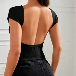 Svart croppad topp med öppen rygg - Trendig svart croppad topp med korta ärmar och helt öppen rygg. Toppens material är stretchigt och följsamt.