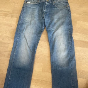 Blå jeansbyxor från Lee - Säljer ett par klassiska blå jeans från Lee i modellen Blake. Byxorna har normal passform, raka ben och fem fickor. De är tillverkade i slitstarkt denim med snygga slitningar framtill och bakfickor med Lee-logga.