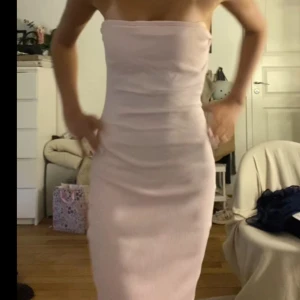 Ljusrosa axelbandslös långklänning - Säljer en ljusrosa axelbandslös långklänning med tight passform. Klänningen har en enkel och stilren design, perfekt för dig som gillar minimalistiskt mode. Materialet ser ut att vara mjukt och följsamt.