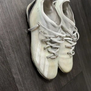 Vita fotbollsskor från Adidas - Säljer ett par vita fotbollsskor från Adidas med snörning och rund tå. Skorna har en lätt och ventilerande ovandel i syntetmaterial och är perfekta för dig som vill ha bra grepp på planen.