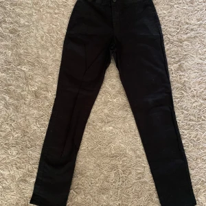 Svarta byxor från Size Needle - Svarta byxor från Size Needle med normal passform och raka ben. Byxorna har knapp och resår i midjan samt fickor bak. Perfekta till många olika outfits och enkla att matcha.