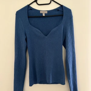 Blå ribbad långärmad topp från H&M - Säljer en blå ribbad långärmad topp från H&M med djup v-ringning. Toppens material är stretchigt och sitter snyggt på kroppen. Perfekt att styla med jeans eller kjol för en enkel och stilren look.